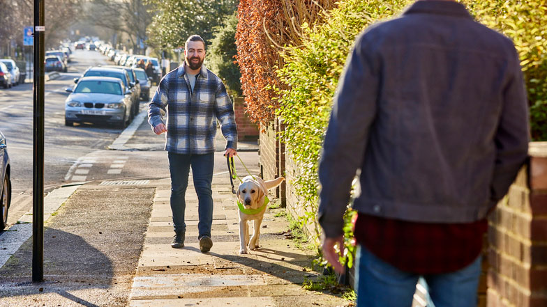 A guide dog owner and his guide dog walk along a pavement together